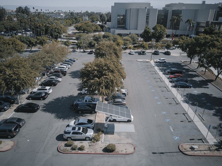 Vue aérienne d'un grand parking arboré avec une ombrière solaire au milieu des voitures