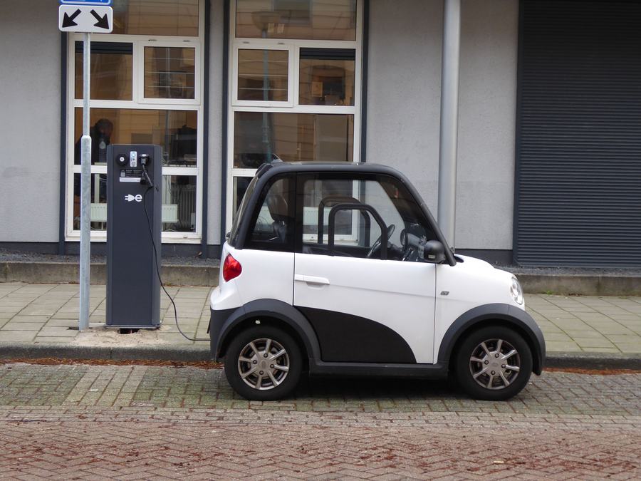 Petite voiture électrique blanche et noire en charge devant une borne, dans une rue pavée